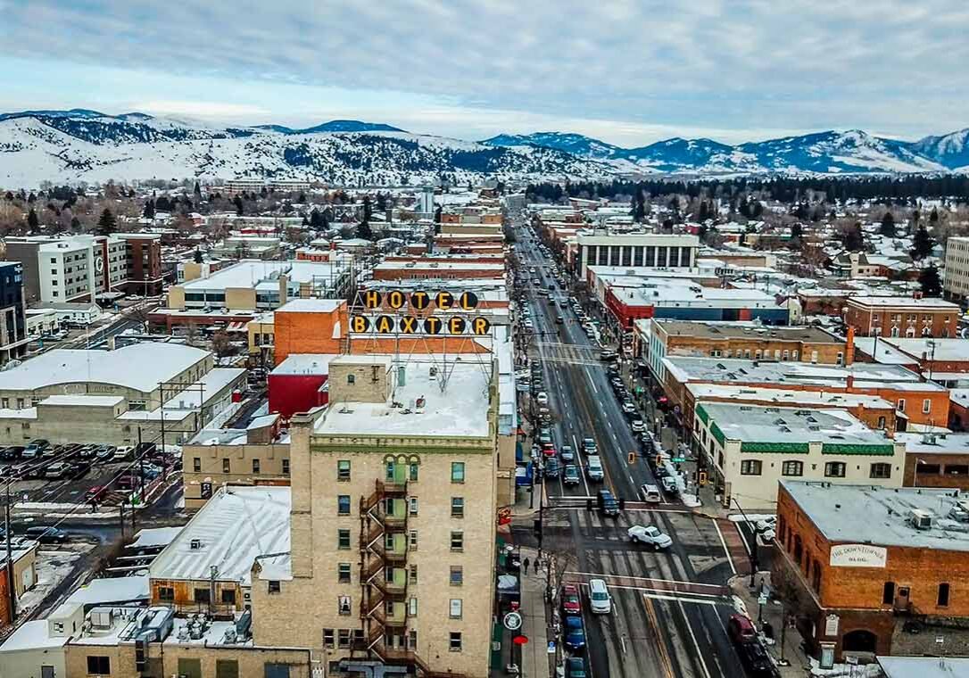 Aerial View of Main Street in downtown Bozeman Montana. Winter snow is scattered on streets and buildings with the mountain range covered in snow in the distance. Famous Baxter Hotel Sign is seen up close.